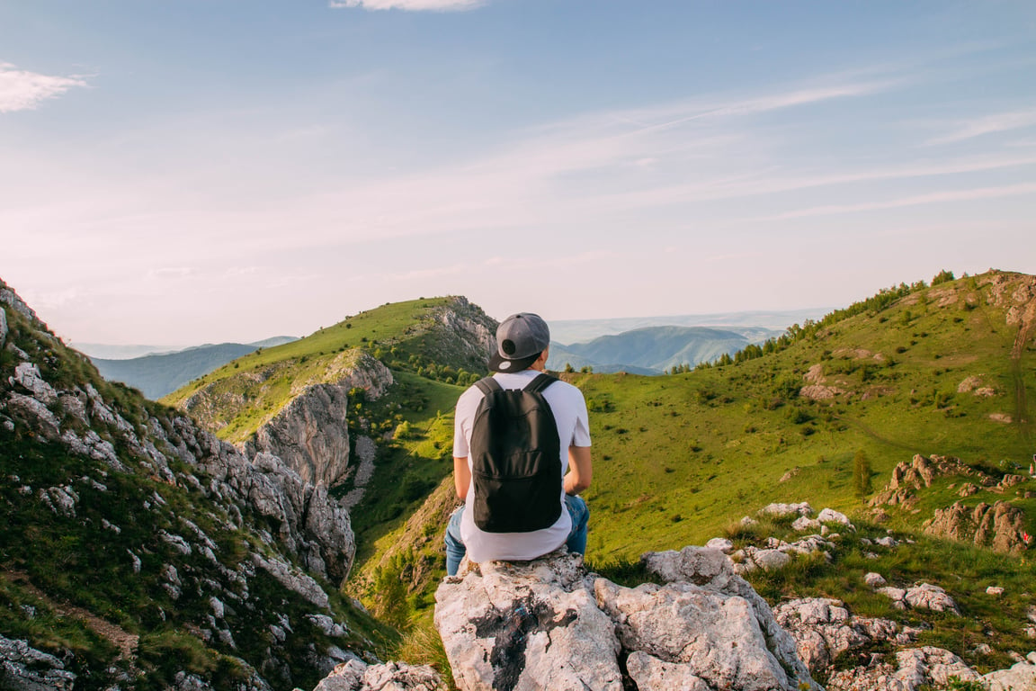 A backpacker seated on a rock on a hill, with a picturesque landscape in the background.