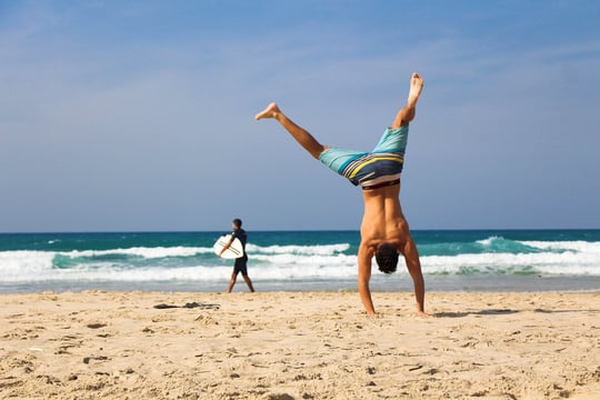 Man performing a cartwheel on a sandy beach with waves in the background.