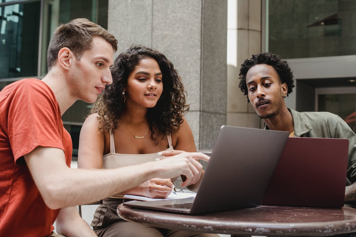 Three professionals collaborating on a project using two laptops at a table.