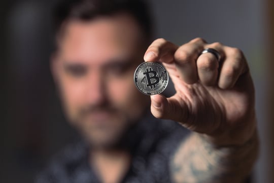 A person holding a coin with the Bitcoin logo.