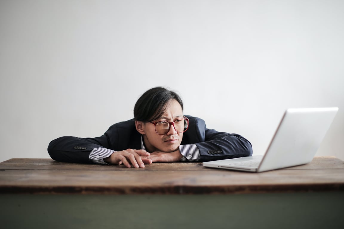 A stressed man laying his head on the desk in front of his laptop.